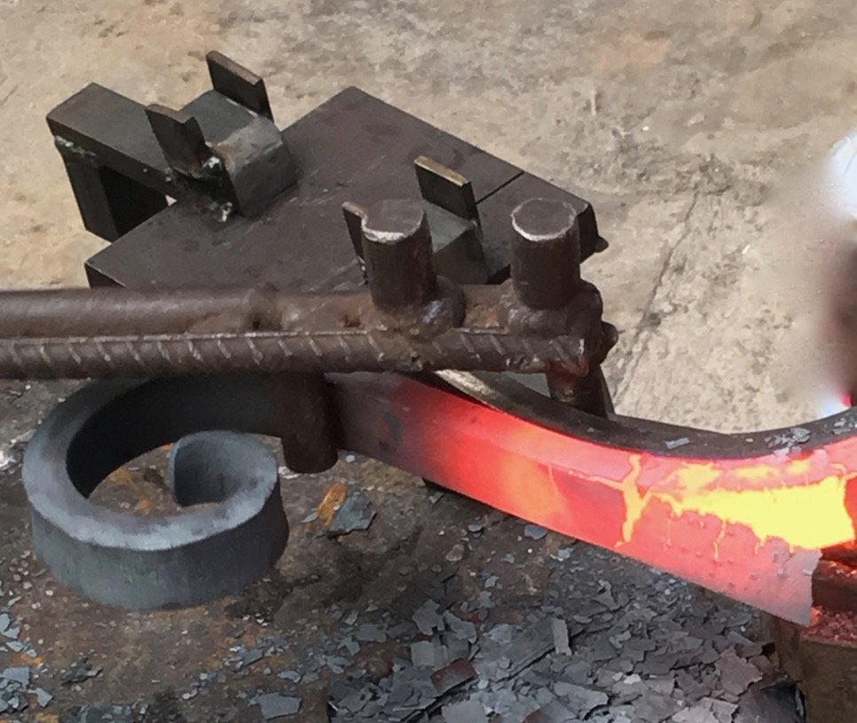 Barra de hierro al rojo vivo doblándose en una voluta en el taller de forja de Kublaikan